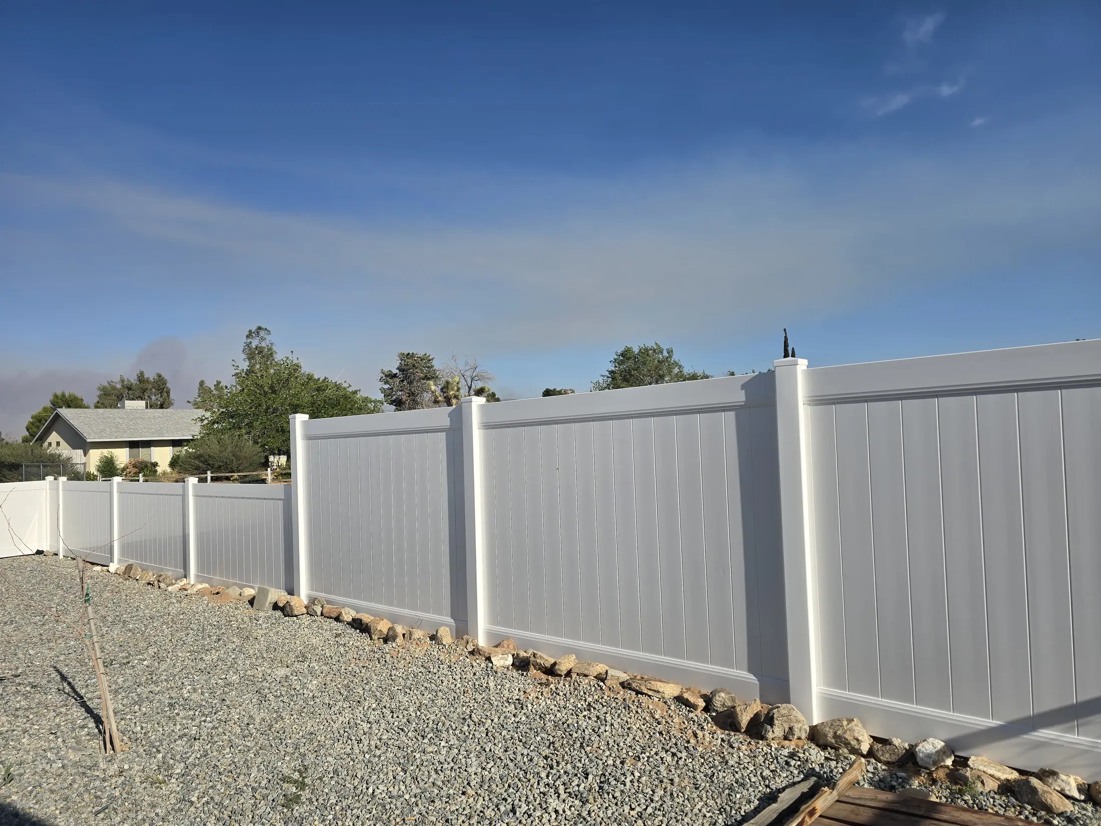 White vinyl privacy fence across a backyard gravel area
