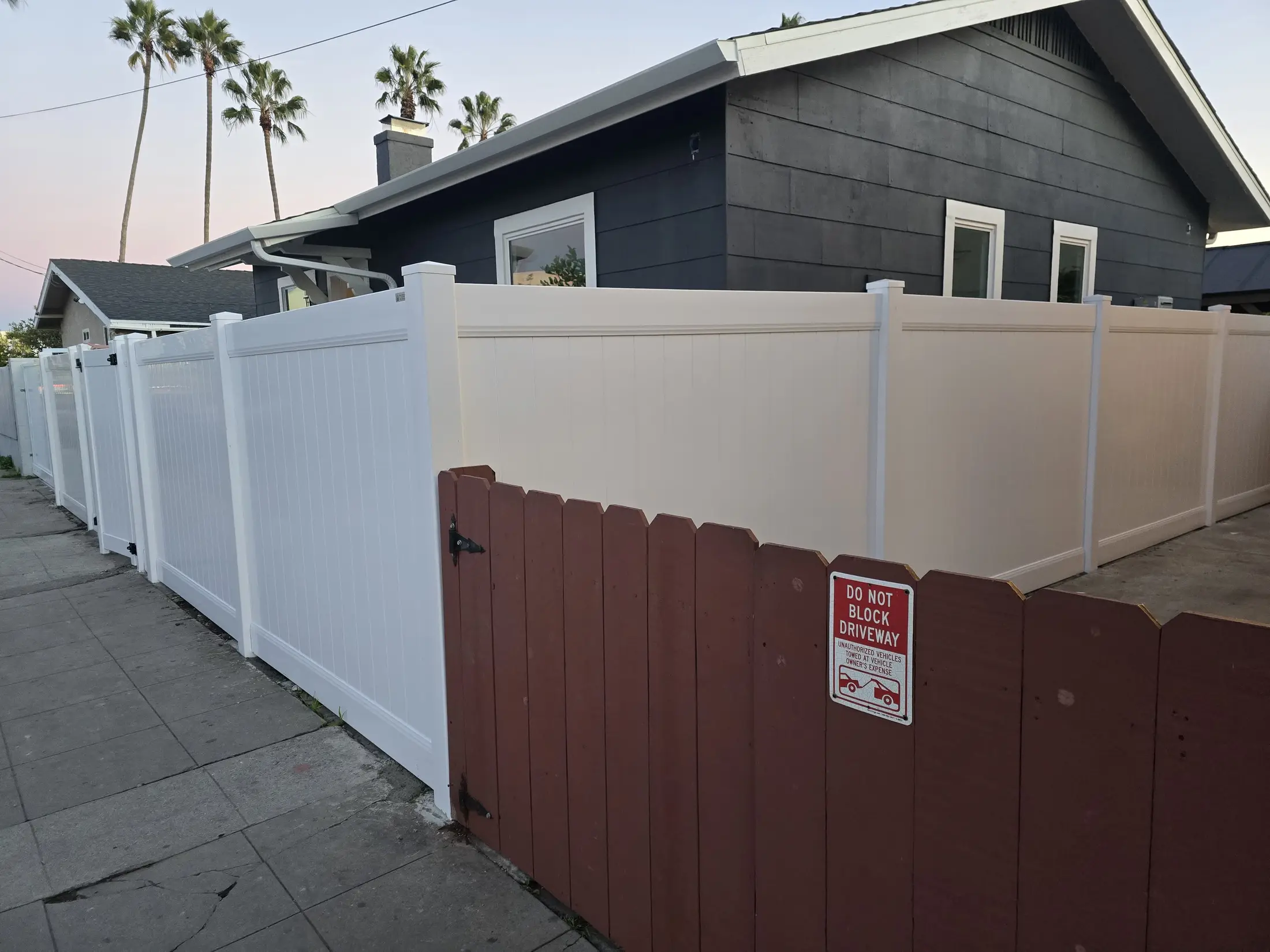 White vinyl privacy fence along a residential sidewalk with gate sections